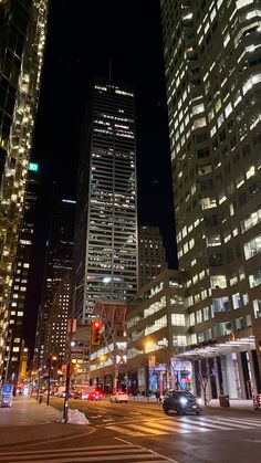 a city street at night with tall buildings in the background and traffic lights on both sides