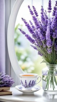 lavender flowers are in a vase next to a cup and saucer