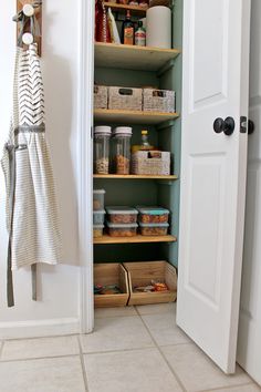 an open pantry door with baskets and food items in the bottom shelf, next to a towel rack