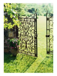 two wrought iron gates in the grass with flowers growing out of one and behind them is a potted plant