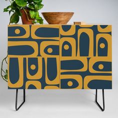 a potted plant sitting on top of a blue and yellow cabinet next to a wooden bowl