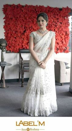 a woman wearing a white sari standing in front of a red flowered wall