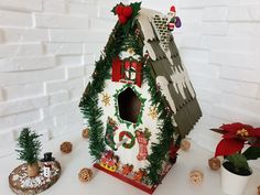 a birdhouse decorated with christmas decorations on a white table next to potted plants