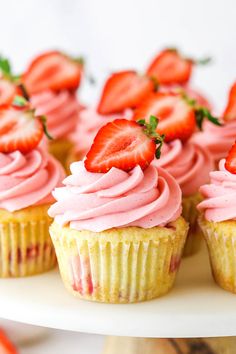 three cupcakes with pink frosting and raspberries on a marble surface