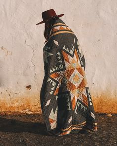 a man with a hat and jacket on standing in front of a wall wearing a cowboy hat