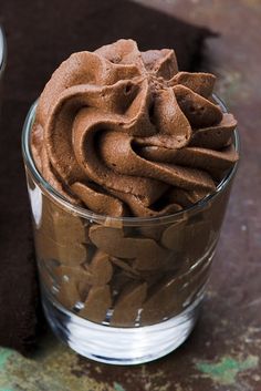 a glass filled with chocolate frosting sitting on top of a brown table next to a napkin