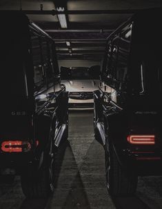 two black trucks parked in a parking garage at night with their lights on and the doors open