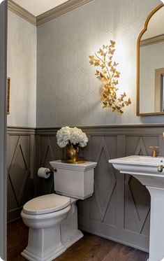 a white toilet sitting next to a sink in a bathroom under a mirror with flowers on it