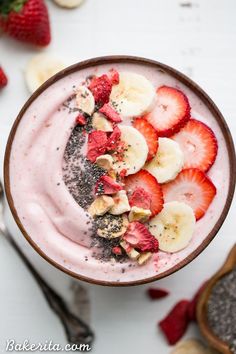 a bowl filled with fruit on top of a white table next to bananas and strawberries