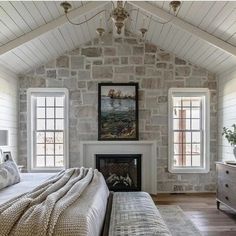 a bedroom with a stone fireplace and two windows in the wall, along with a white bed