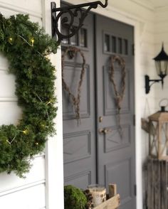 two wreaths hanging on the front door of a house with lights strung from them