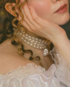 a woman in a white dress with pearls on her neck and hand near her face