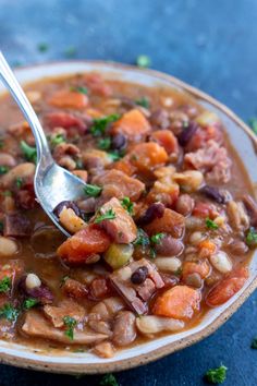 a bowl filled with beans and vegetables on top of a blue tablecloth next to a spoon