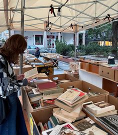 a woman is looking at books on display in a book sale area under a tent