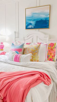 a white bed topped with lots of pillows next to a painting on the wall above it