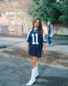 a woman standing in the street wearing a football jersey and white boots with her hands on her hips