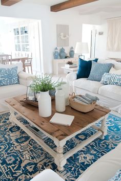 a living room filled with white furniture and blue rugs on top of a wooden table