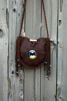 This leather tote has a beaded eagle surrounded by the four directions beadwork and measures 10 inches tall x 10 inches wide x 2 / 3/4 inches deep. This soft brown leather tote has tied fringe down the sides of the bag that are decorated with turquoise blue glass crow beads. This shoulder bag has an antler toggle for a closure. The comfortable crossbody strap measures 48 inches. If you would like to have your strap longer or shorter feel free to ask we are happy to make this change for you. This Brown Hand-stitched Tote Shoulder Bag, Brown Hand-stitched Crossbody Bag, Leather Mobile Phone Bag For Festivals, Handmade Leather Festival Bag, Festival Tote Shoulder Bag With Hand-stitched Details, Leather Tote Bag For Festival, Brown Festival Bag With Removable Pouch, Soft Leather Shoulder Bag For Festivals, Festival Crossbody Shoulder Bag With Hand-stitching