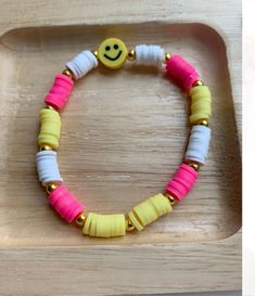 a yellow smiley face beaded bracelet with white and pink beads on a wooden tray