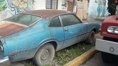 an old blue car parked next to a red truck on the side of the road