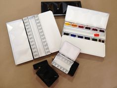 an assortment of watercolor paints and brushes on a table with other paint samples in their trays