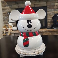 a white ceramic bear with a red hat and scarf on it's head sitting on a table in front of a fireplace