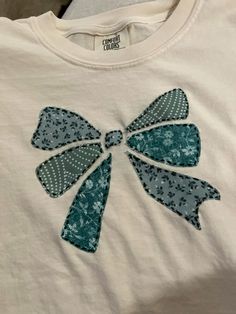 a white t - shirt with blue bows on the front and green bow on the back