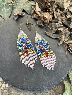 two pairs of beaded earrings sitting on top of a rock next to some leaves