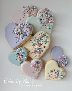 several decorated heart shaped cookies with sprinkles and pearls on them, all in pastel colors