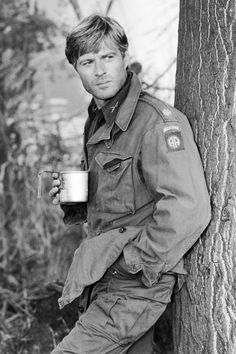 a man in uniform is holding a cup and leaning against a tree with the words robert redford on it