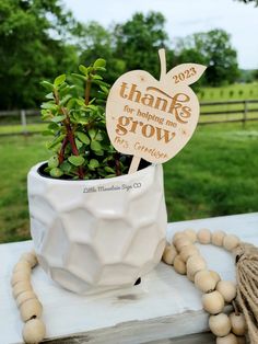 a small plant in a white ceramic pot with a wooden sign that says thank for helping me grow