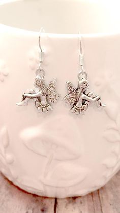 a pair of silver earrings sitting on top of a wooden table next to a cup