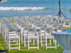 rows of white folding chairs sitting on top of a lush green field next to the ocean