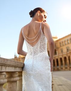 a woman in a wedding dress leaning against a stone wall looking at the sky with her back to the camera