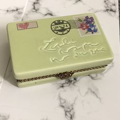 a green box sitting on top of a marble counter next to a postage stamp holder