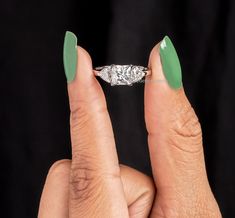 a woman's hand holding a diamond ring with green nail polish on her fingers