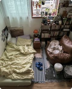 a messy bedroom with a bed, chair and bookshelf in the corner next to a window