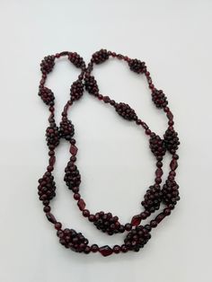 a long beaded necklace with red beads on a white surface, including an oval clasp