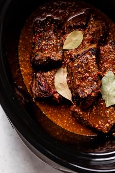 a close up of some food in a crock pot with leaves on the side