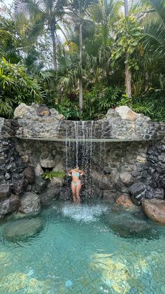 a woman is standing in the middle of a pool surrounded by rocks and palm trees