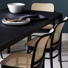 a black table with chairs and a bowl on it, next to a white plate