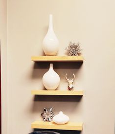 three wooden shelves with white vases and other decorative items on them in a room