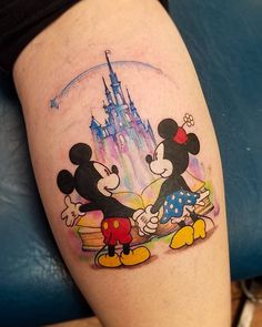 a couple of mickey and minnie mouse tattoos on the leg, with a castle in the background