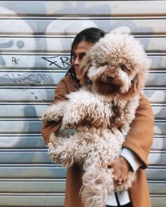 a woman holding a dog in front of a graffiti covered garage door with her arms wrapped around the dog