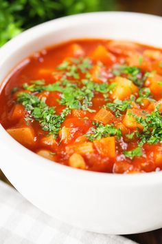 a white bowl filled with soup and garnished with parsley in it on top of a table