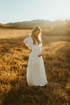 a woman standing in the middle of a field wearing a white dress and holding her hands on her hips