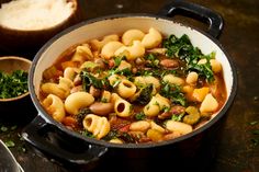 a pot filled with pasta and greens next to bread