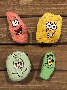 three rocks with cartoon faces painted on them sitting on a wooden surface next to each other