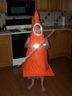 a young child wearing an orange costume standing in a kitchen with wooden floors and cabinets