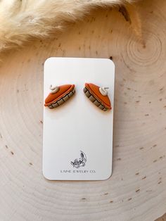 an orange and white pair of earrings sitting on top of a piece of wood